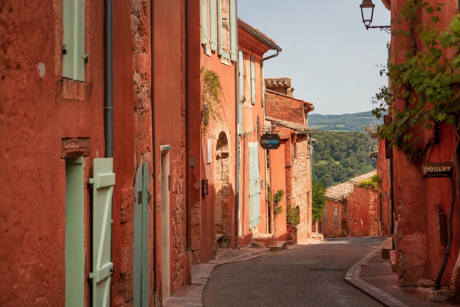 Façades ocres et volets pastel de Roussillon dans une rue en pente pavée, lumière chaude de fin d'après-midi